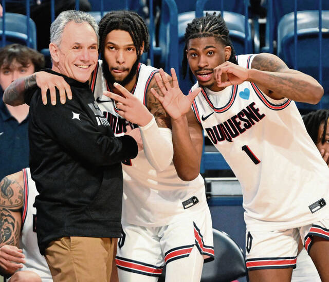 Duquesne’s Dae Dae Grant and Jimmy Clark III (1) celebrate with coach Keith Dambrot after beating George Mason for the coach’s 500th win Wednesday, Feb. 8, 2023, at UPMC Cooper Fieldhouse.