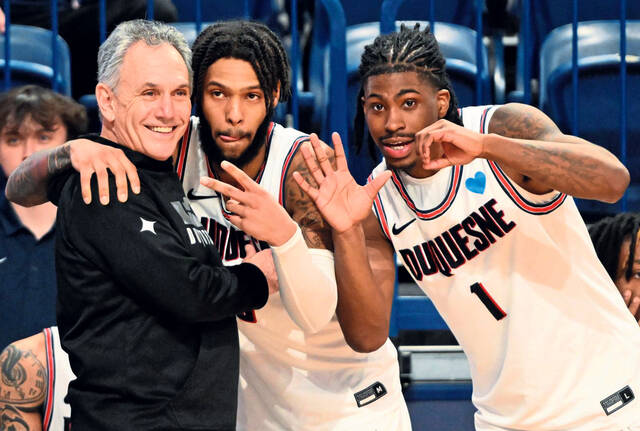 Duquesne’s Dae Dae Grant (center) and Jimmy Clark III celebrate with head coach Keith Dambrot after beating George Mason for coach’s 500th win in February 2023 at UPMC Cooper Fieldhouse.